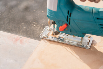 Close-up hands of a male builder cuts a wooden with an electric jigsaw. sawdust fly to sides.