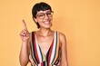 Beautiful brunettte woman wearing casual clothes and glasses pointing finger up with successful idea. exited and happy. number one.