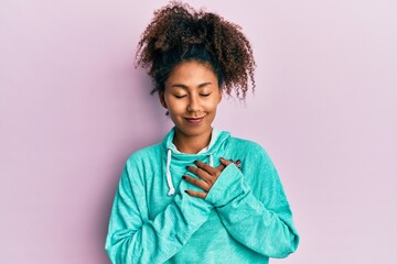 Beautiful african american woman with afro hair wearing casual sweatshirt smiling with hands on chest with closed eyes and grateful gesture on face. health concept.