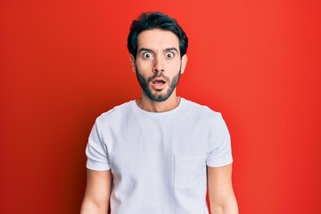 Canvas Print - Young hispanic man wearing casual white tshirt afraid and shocked with surprise and amazed expression, fear and excited face.