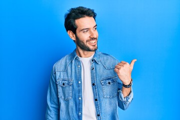 Sticker - Young hispanic man wearing casual clothes pointing thumb up to the side smiling happy with open mouth