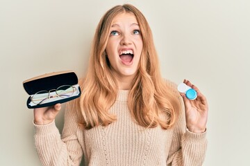 Wall Mural - Beautiful young caucasian girl holding glasses and contact lenses angry and mad screaming frustrated and furious, shouting with anger looking up.