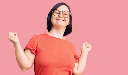 Canvas Print - Brunette woman with down syndrome wearing casual clothes and glasses very happy and excited doing winner gesture with arms raised, smiling and screaming for success. celebration concept.