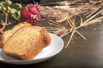 Two slices of banana bread on a small plate with a wooden chopping board and garnish with flowers and straw