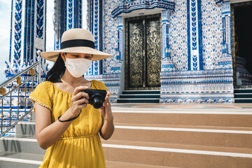 Wall Mural - New normal travel of traveler asian woman with mask and camera sightseeing in temple Thailand