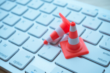 Maintenance, repair, under construction in computer system from virus or ransomware concept. Close up orange white traffic warning cones or pylon on keyboard computer background with copy space.