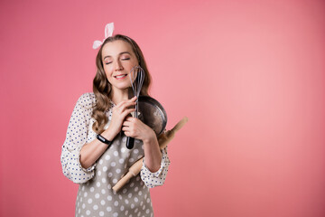 Young happy pastry chef woman with kitchen baking utensils in her hands. A cook in a polka-dot apron. pastry chef in an apron on a pink background.