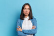 © WHstudio Leushin N - Portrait of displeased offended young Asian woman with dark hair keeps arms folded looks angrily aside doesnt agree with somebodys opinion wears neat clothes isolated over blue studio background