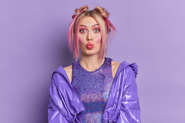 Retro styled fashionable young woman with bright makeup dressed in stylish purple clothes keeps lips rounded has trendy hairstyle isolated over vivid violet background prepares for disco party