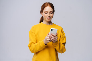 smiling lovely young woman wearing stylish yellow sweater texting on her cell phone on isolated whit