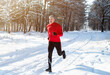 Leinwandbild Motiv Athletic mature man in sportswear jogging at snowy winter park. Healthy senior runner sprinting outdoors in cold weather