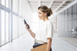 © ImageFlow - Young woman with smartphone and books in office