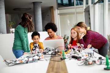 Wall Mural - Happy kids with their African American female science teacher with laptop programming electric toys and robots at robotics classroom