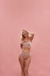 Playful mood. Excited middle aged caucasian blonde woman wearing underwear keeping eyes closed and smiling while posing isolated over pink background