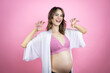 Young beautiful brunette woman pregnant expecting baby over isolated pink background smiling funny doing claw gesture as cat, aggressive and sexy expression