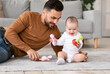 © Prostock-studio - Dad Playing With Little Baby Toddler Holding Toys Sitting Indoors