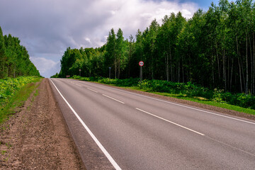 An asphalted intercity road with white markings extending into the distance through a green forest.