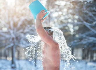 Mature man pouring icy water from bucket onto his head at snowy winter forest. Developing resistance to cold