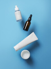 Beauty levitation concept with cream tube, jar and serum on blue background