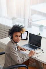 Wall Mural - Vertical portrait of teenage African-American boy wearing headset and looking at camera while using laptop at home, young gamer or blogger concept, copy space