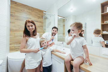 young happy family man, woman and two small children, two boys in a backpack brushing teeth together