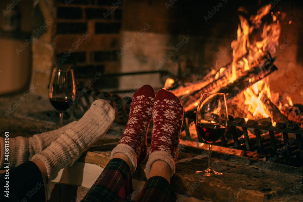 Cosy winter evening. Drinking wine and reading book next to fireplace. - obrazy, fototapety, plakaty 