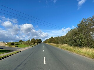 View along, Highmoor Lane, with grass verges, trees, and a blue sky in, Clifton, Brighouse, UK