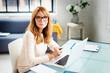 © sepy - Portrait shot of smiling mature woman using laptop while sitting at desk in her sitting room and working from home. Home office.