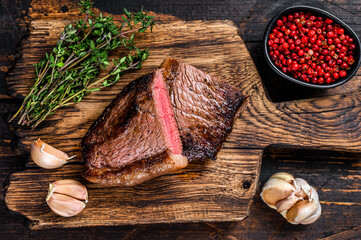 Wall Mural - Cut fried rump cap or brazilian picanha beef meat steak on a wooden board. Dark wooden background. Top view