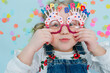© zzzdim - Happy little blonde girl pressing happy birthday glasses to her face. Top view. Funny face.