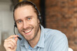 Smiling young office worker wearing a headset and looking at the camera, a positive blue-eyed man with the beard working in the customer service department, making and receiving calls