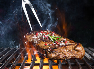 Tasty beef steak on cast iron grate with fire flames. Barbecue concept.