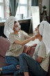 © pressmaster - Cute female twins with towels on heads and facial clay mask relaxing after bath