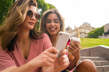 Two friends using mobile phone outdoors.