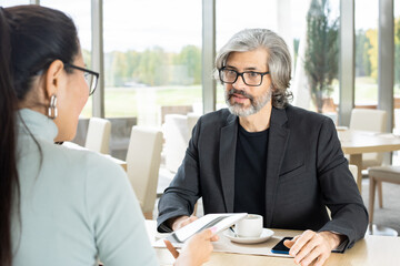 Wall Mural - Serious mature businessman answering question of his young female colleague