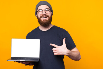Cheerful handsome bearded man pointing at empty blank screen on laptop.