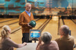 Portrait of happy senior man smiling at group of friends while playing bowling together at entertainment center, copy space