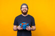 Portrait of charming young man with beard holding gift box over yellow background.