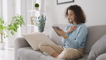 Wall Mural - Happy hispanic teen girl waving talking using digital tablet enjoying online virtual chat video call with friends or family in distance chat virtual meeting using pad computer sitting on sofa at home.