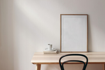 Breakfast still life scene. Cup of coffee, books and empty picture frame mockup on wooden desk, table. Elegant working space, home office concept. Scandinavian interior design. Room in sunlight.