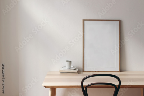 Breakfast still life scene. Cup of coffee, books and empty picture frame mockup on wooden desk, table. Elegant working space, home office concept. Scandinavian interior design. Room in sunlight. © tabitazn