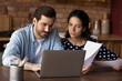 © fizkes - Young Caucasian couple look at laptop screen manage family financial paperwork paying bills online. Millennial man and woman work on computer, use web banking system for payment on gadget.