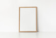 © Candle photo - Empty wooden frame stands on white table against wall. Mockup poster frame close up in home interior.