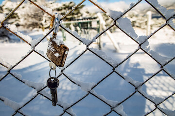 rusty lock suspended on a snow-covered wire mesh, with a key underneath