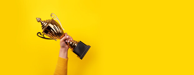 woman holding up a gold trophy cup as a winner in a competition, panoramic image