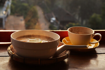 Hot boiled rice in a white tile cup, placed on a wooden floor with a mist and mountain in the morning as a background.