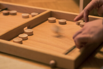 Wooden bard game where you shoot round wooden blocks through opening with help of an elastic band. Two players visible.