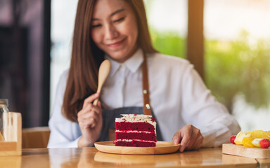 Wall Mural - Closeup image of a beautiful woman, female chef baking and eating a piece of red velvet cake in wooden tray