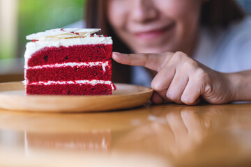 Wall Mural - Closeup image of a beautiful young asian woman looking and touching a piece of red velvet cake in wooden tray on the table