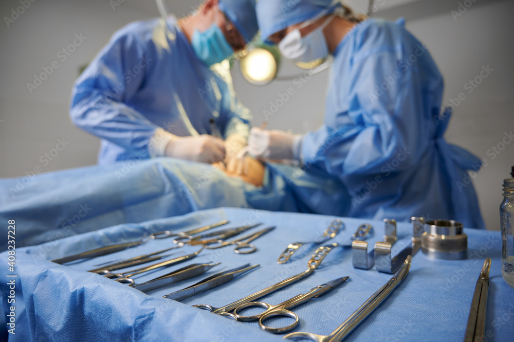 Plastic surgery instruments on surgical table with medical team and patient on blurred background. Doctor and assistant performing aesthetic surgery. Concept of plastic surgery and medical instruments - obrazy, fototapety, plakaty 